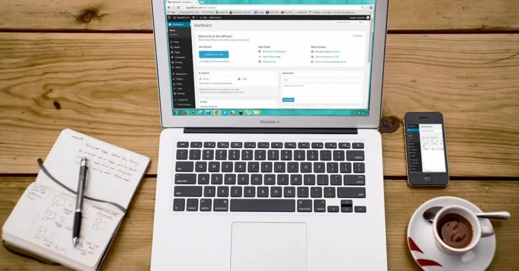 Turned-on Macbook Air Beside Black Iphone 4, Cup of Tea, and Notebook on Brown Wooden Surface